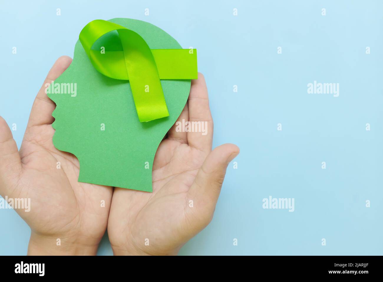 Hand hält das menschliche Kopfprofil mit einem hellgrünen Bewusstseinsband am Gehirn. Lyme-Borreliose, Psychose, psychische Erkrankungen im Kindesalter, Lymphom und postpartum Stockfoto