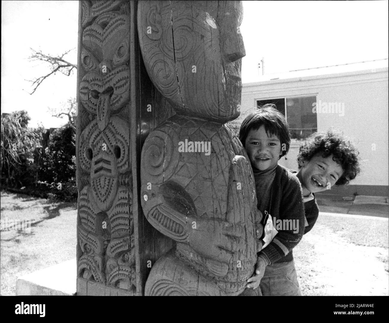 Zwei Maori-Kinder spielen neben einer übergroßen, geschliffen Statue eines Gottes oder Dämons der Maori-Kultur. Stockfoto