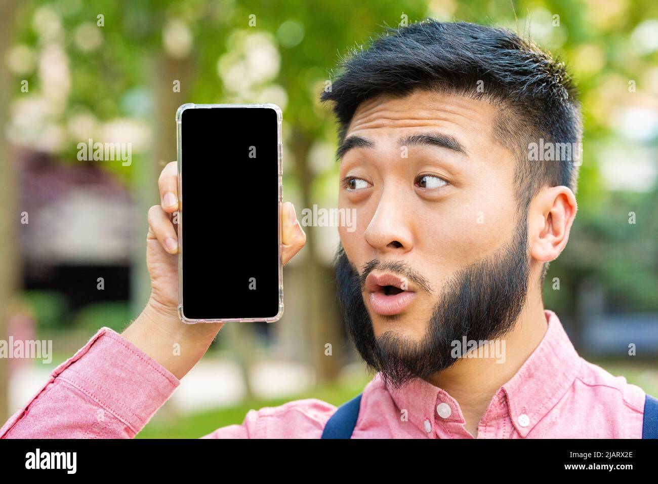 Mann mit einem überraschten Gesicht, das den Bildschirm des Handys zeigt Stockfoto