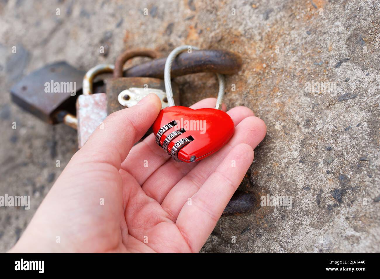 Ein rotes herzförmiges Kombinationsschloss mit der Hand an der Betonwand. Stockfoto