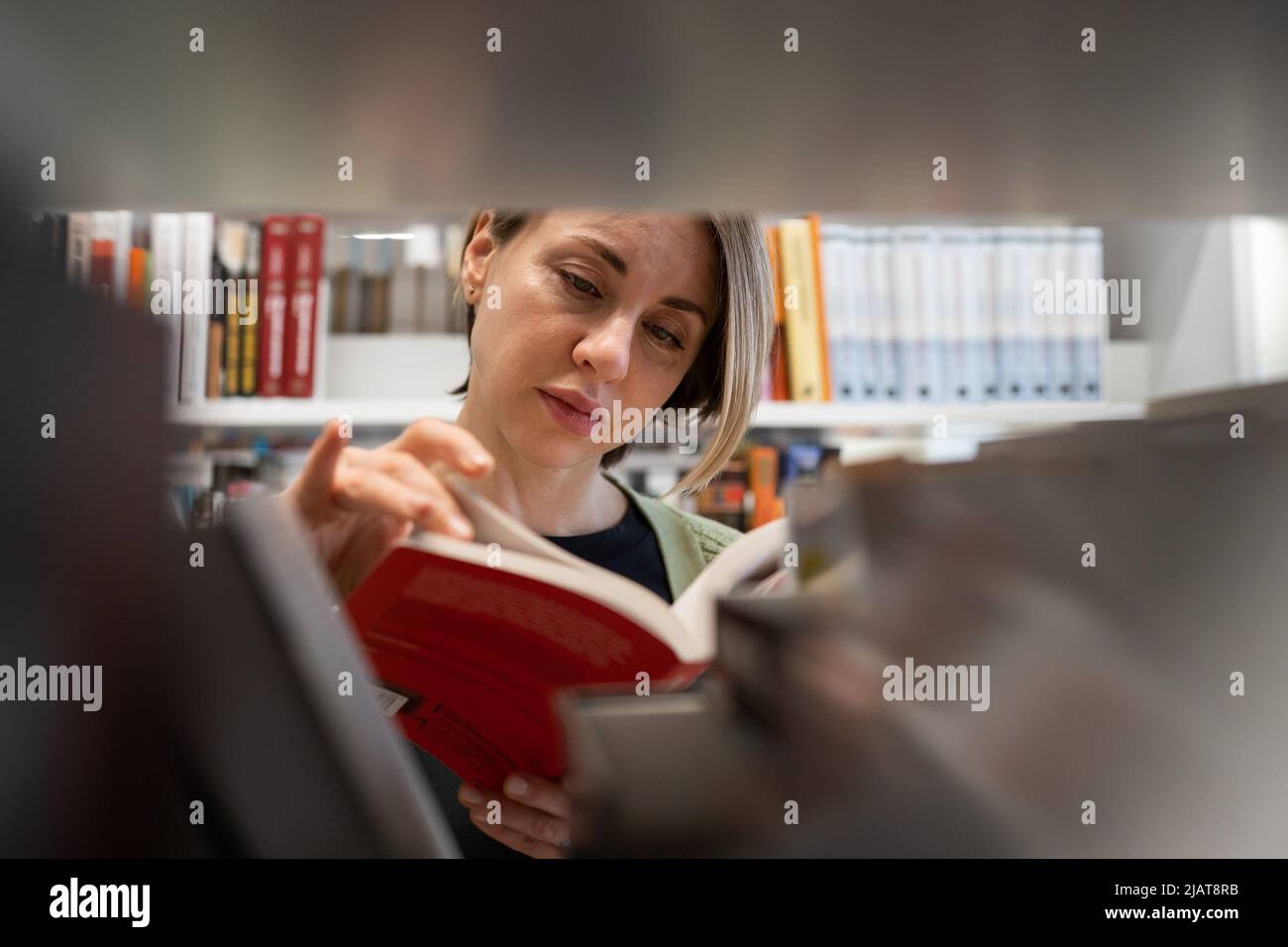 Skandinavische Frau mittleren Alters, die Lehrbuch wählt, auf der Suche nach Literatur während der Vorbereitung auf die Prüfung Stockfoto