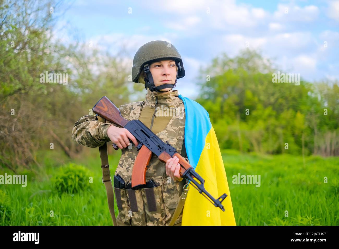 Porträt einer Soldatinnen mit Gewehr und ukrainischer Flagge auf der Schulter, die wegschaut Stockfoto