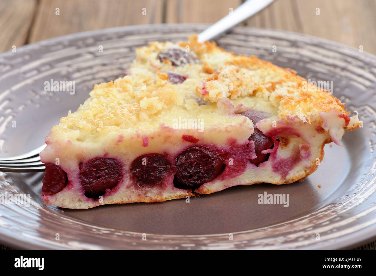 Stück hausgemachter leckerer Clafoutis-Kuchen mit ganzen Kirschen auf braunem Teller aus der Nähe Stockfoto