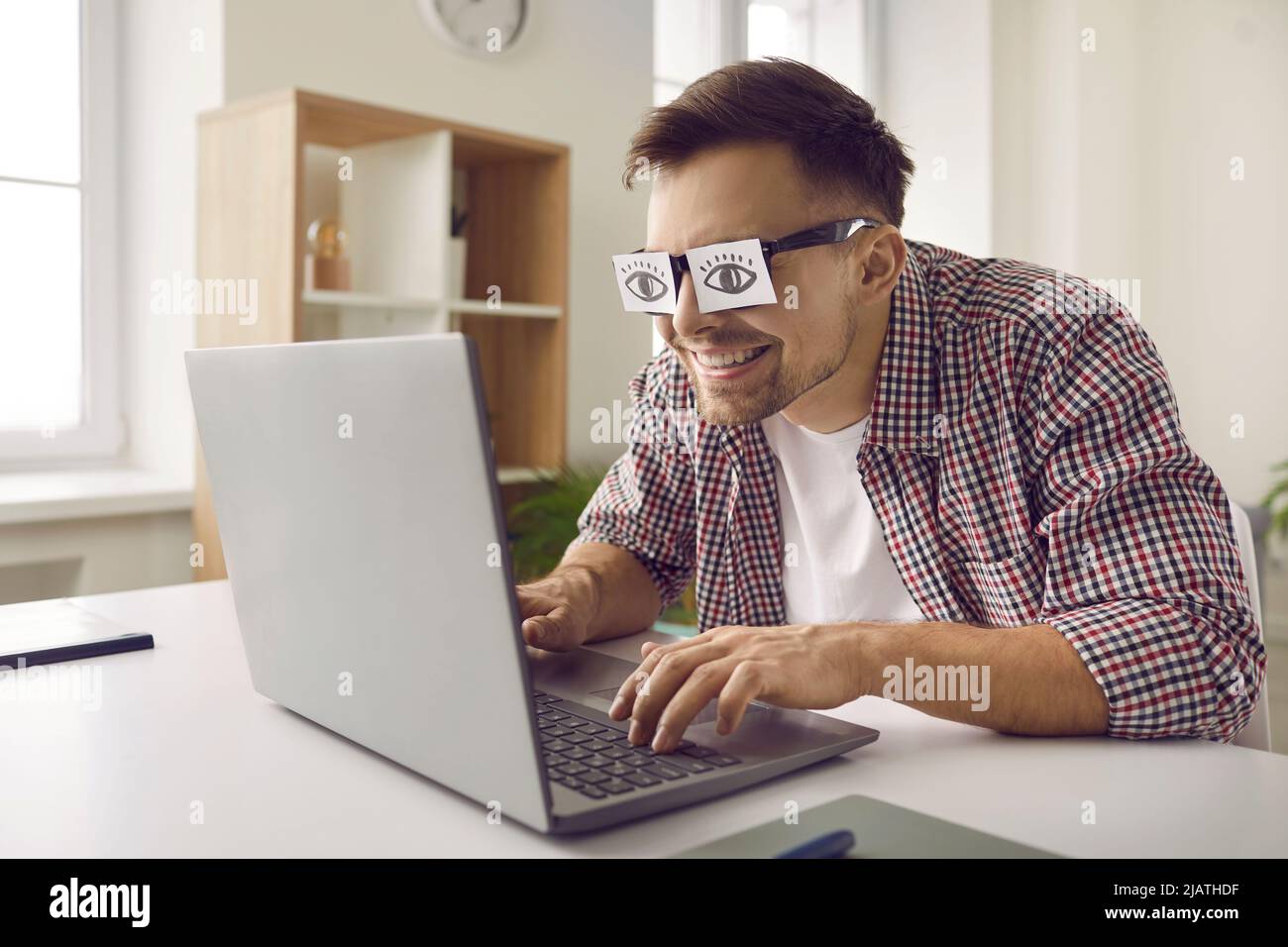 Seltsamer, müde, schlamvoller Mann mit lustigen Papieraufklebern, die auf einem Laptop-Computer arbeiten Stockfoto