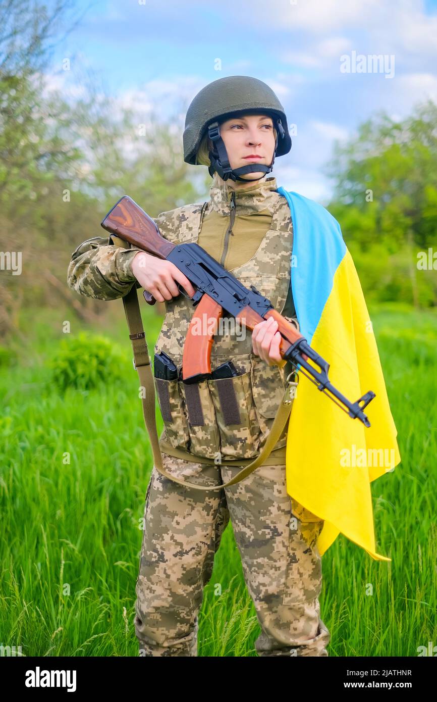 Soldatin mit Gewehr und ukrainischer Flagge auf der Schulter, die wegschaut Stockfoto