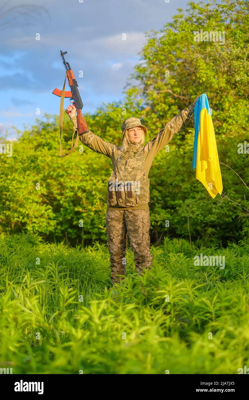 Soldatin mit Waffe und ukrainischer Flagge in erhobenen Armen, die wegschaut Stockfoto