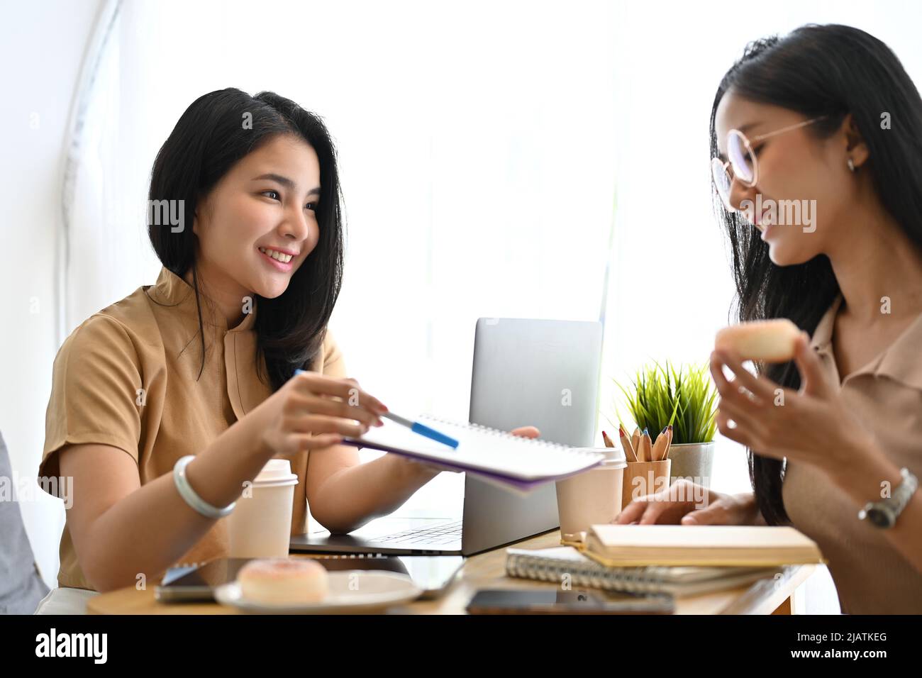 Glückliche und charmante asiatische junge Frau, die ihrem College-Freund im Café Nachhilfe für Mathematik und Naturwissenschaften lehrt. Stockfoto