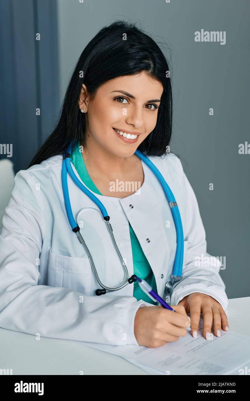 Arztberuf. Lächelnde Hausärztin sitzt in medizinischer Uniform am Arbeitsplatz Stockfoto