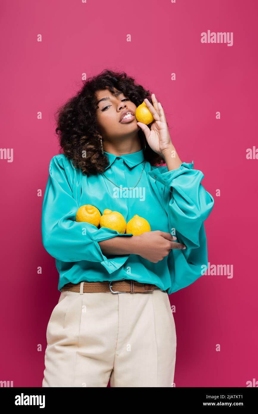 Hübsche afroamerikanische Frau in trendiger Bluse mit Zitronen isoliert auf rosa Stockfoto