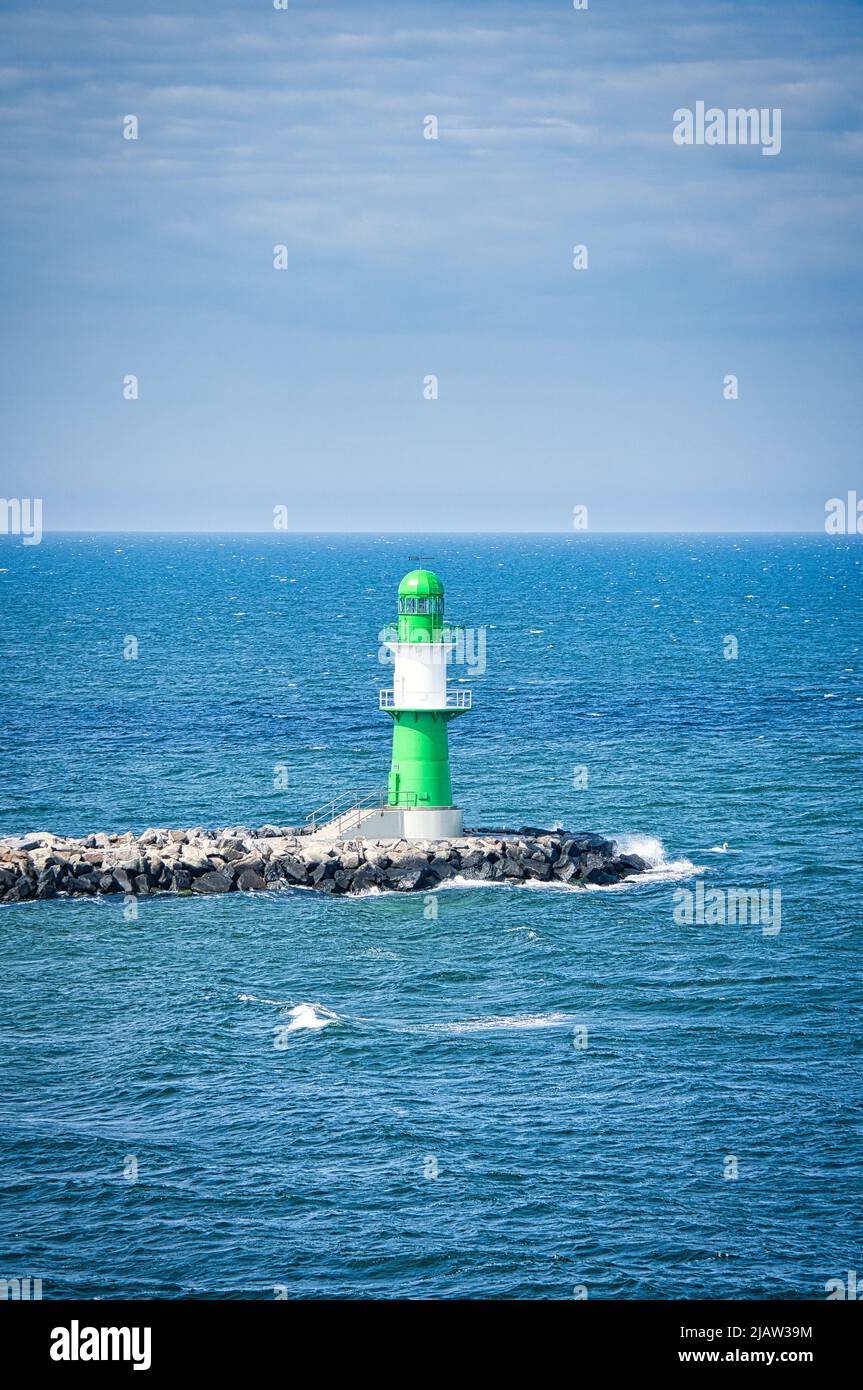 Grün-weißer Leuchtturm an der Warnow in Rostock an der Ostsee. Wahrzeichen der Stadt. Wellen am Steinrand. Landschaftsfoto aus Deutschland Stockfoto