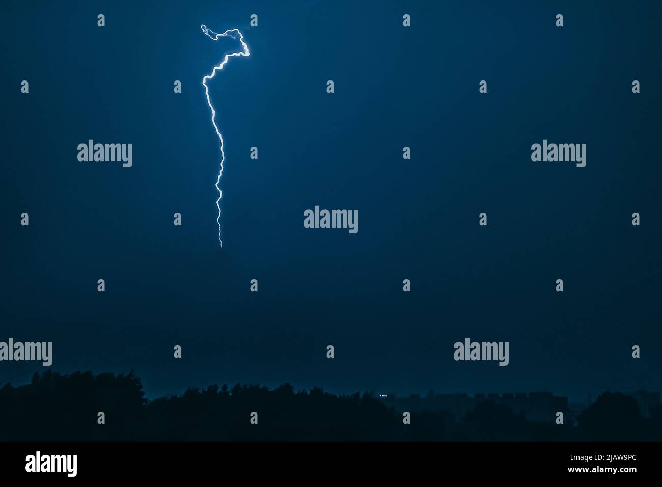 Blitz im Himmel über der Stadt. Helle Blitze in dunkler Nacht. Gewitterwolken und Elektrizität entlädt sich in der Atmosphäre. Nächtliches Stadtbild. Stockfoto
