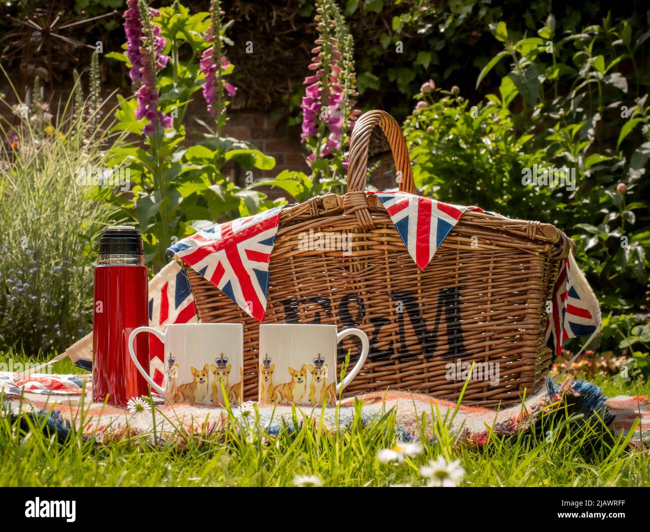 Picknickkorb aus Korbkörbchen mit zwei Jubiläumsbechern aus Platin und einer roten Flasche auf Gras im Freien Stockfoto