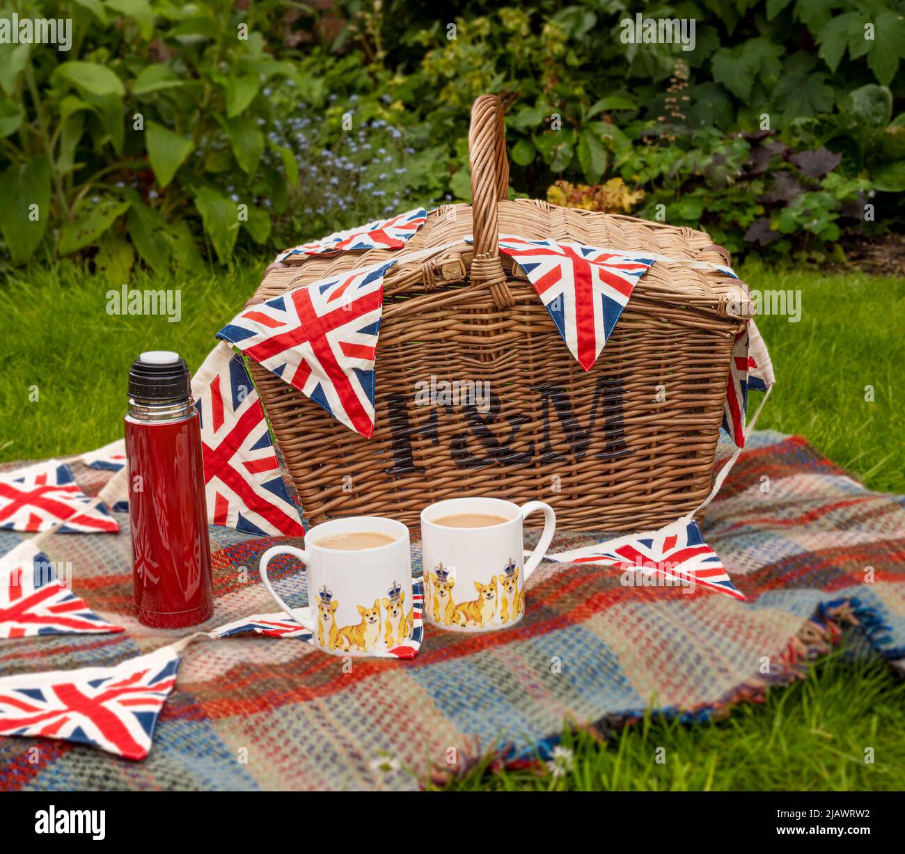 Picknickkorb aus Korbkörbchen mit zwei Jubiläumsbechern aus Platin und einer roten Flasche auf Gras im Freien Stockfoto