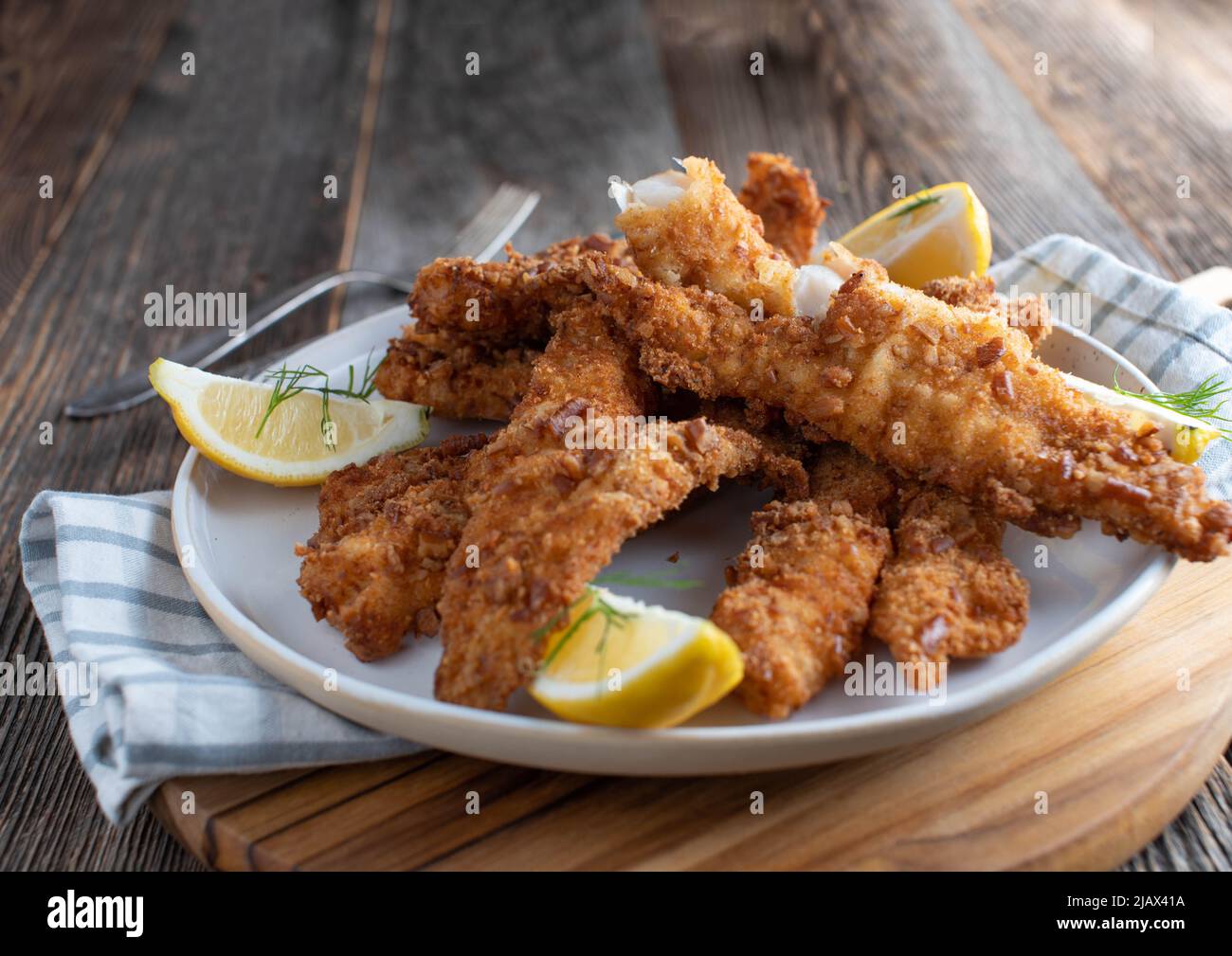 Knusprig gebratener Fisch auf einem Teller mit Zitrone. Auf Holztisch isoliert serviert. Nahaufnahme mit Kopierbereich Stockfoto