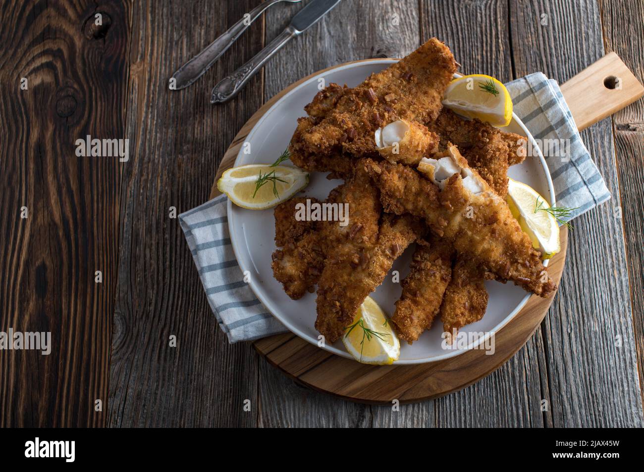 Frittiertes Fischfilet mit Brezelbreadierung. Serviert auf einem Teller mit Zitrone isoliert auf Holztisch Hintergrund. Draufsicht Stockfoto