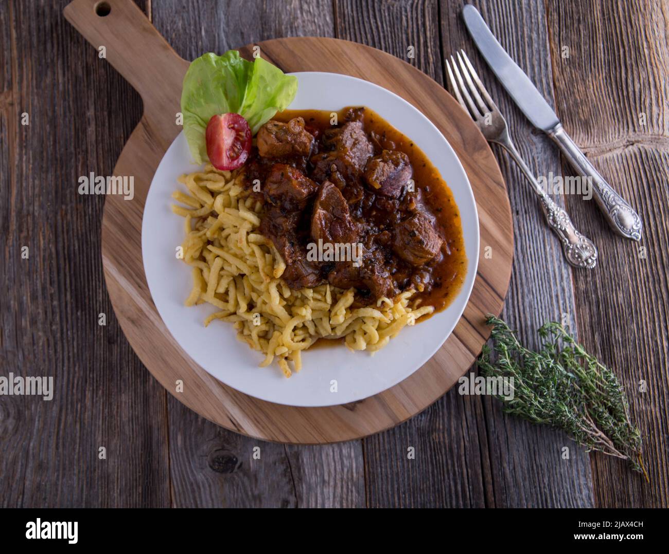 Gulasch mit spätzle Nudeln auf einem Teller isoliert auf Holztisch mit Kopieplatz Stockfoto