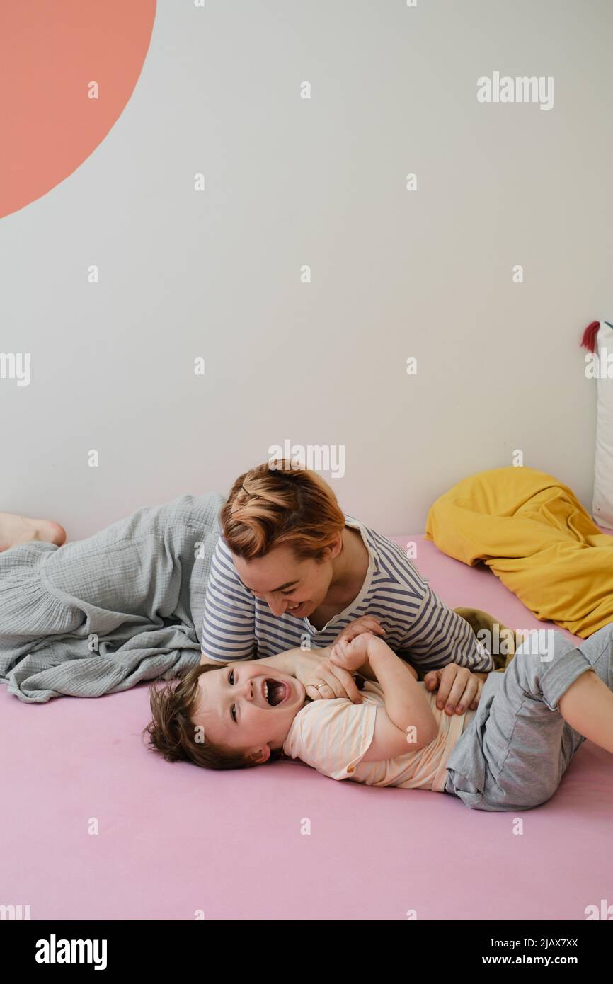 Mutter hat Spaß mit Sohn auf dem Bett. Mutter und Kleinkind spielen, kitzeln ein Kind, lachen am Morgen. Positive Emotionen nach dem Schlaf. Aufwachendes Kind Stockfoto