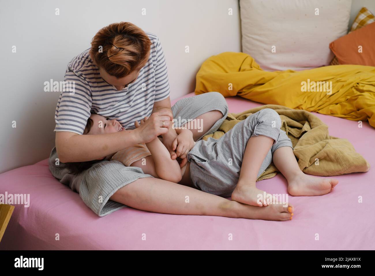 Mutter hat Spaß mit Sohn auf dem Bett. Mutter und Kleinkind spielen, kitzeln ein Kind, lachen am Morgen. Positive Emotionen nach dem Schlaf. Aufwachendes Kind Stockfoto