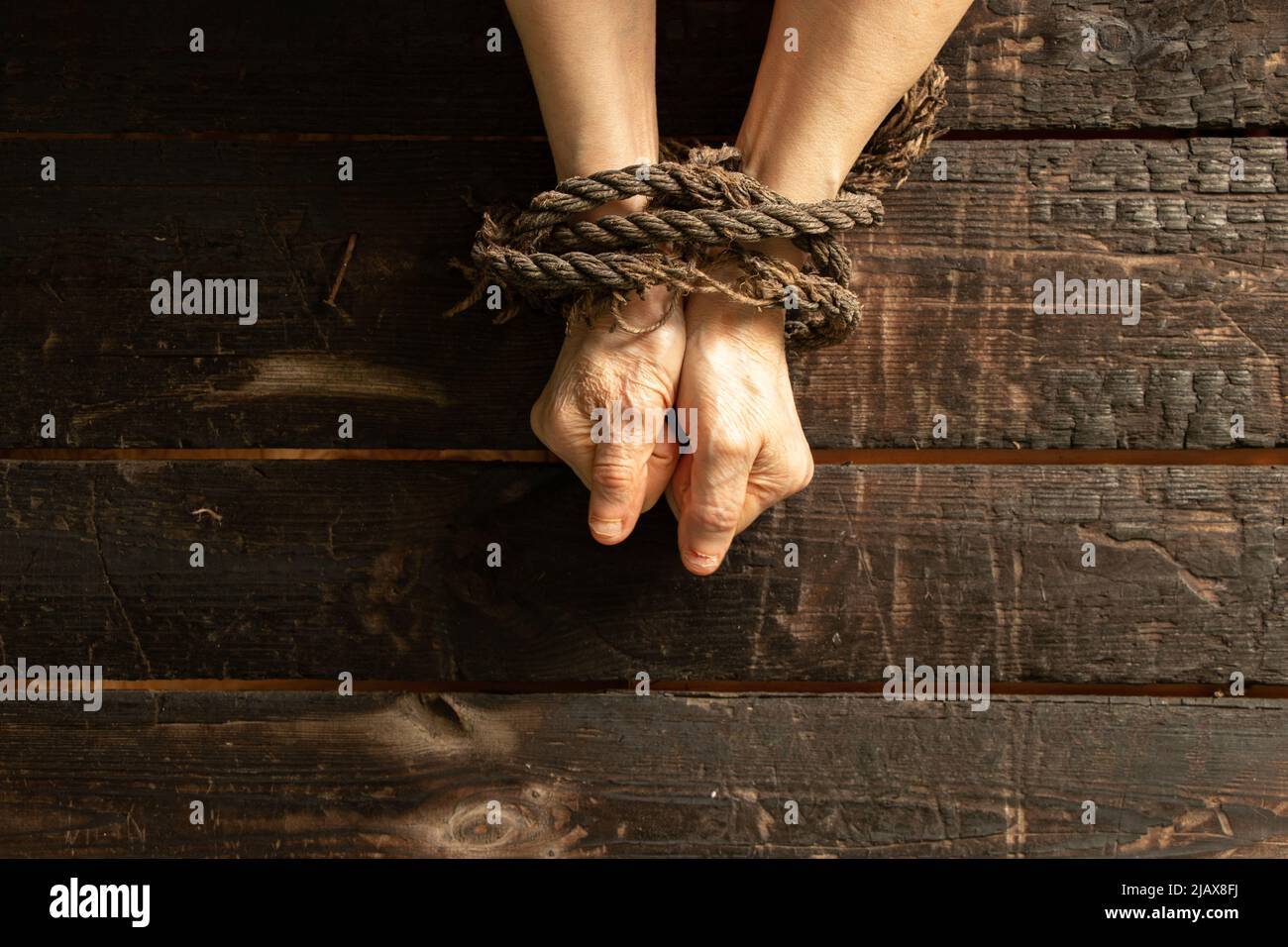 Gefesselt die Hände einer alten Frau mit einem Seil auf einem Holztisch, Mangel an Macht über die Menschen, Sklave Stockfoto
