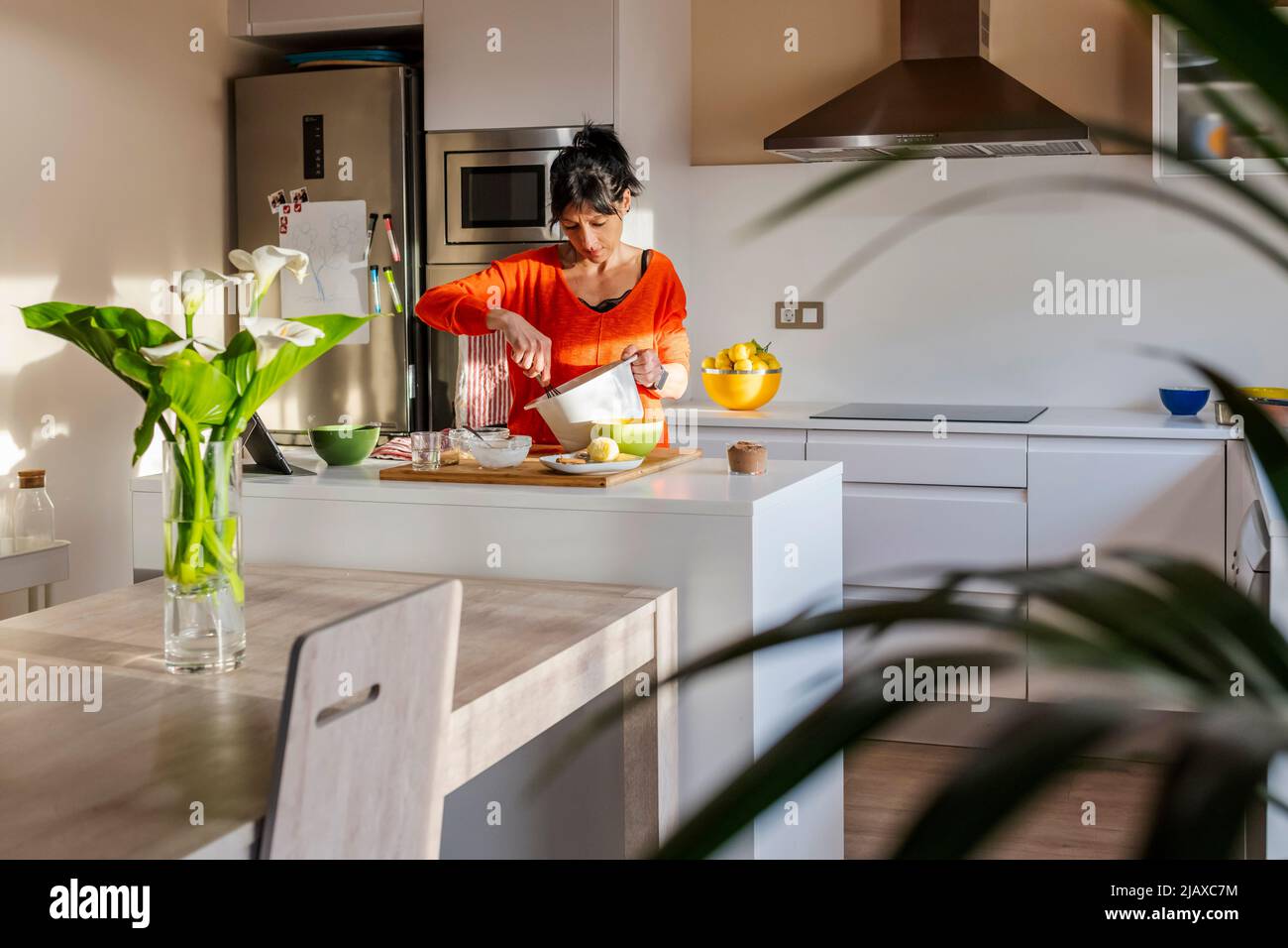 Frau in orangefarbenem Pullover, die Eier auf einer weißen Schale hastert. Stockfoto