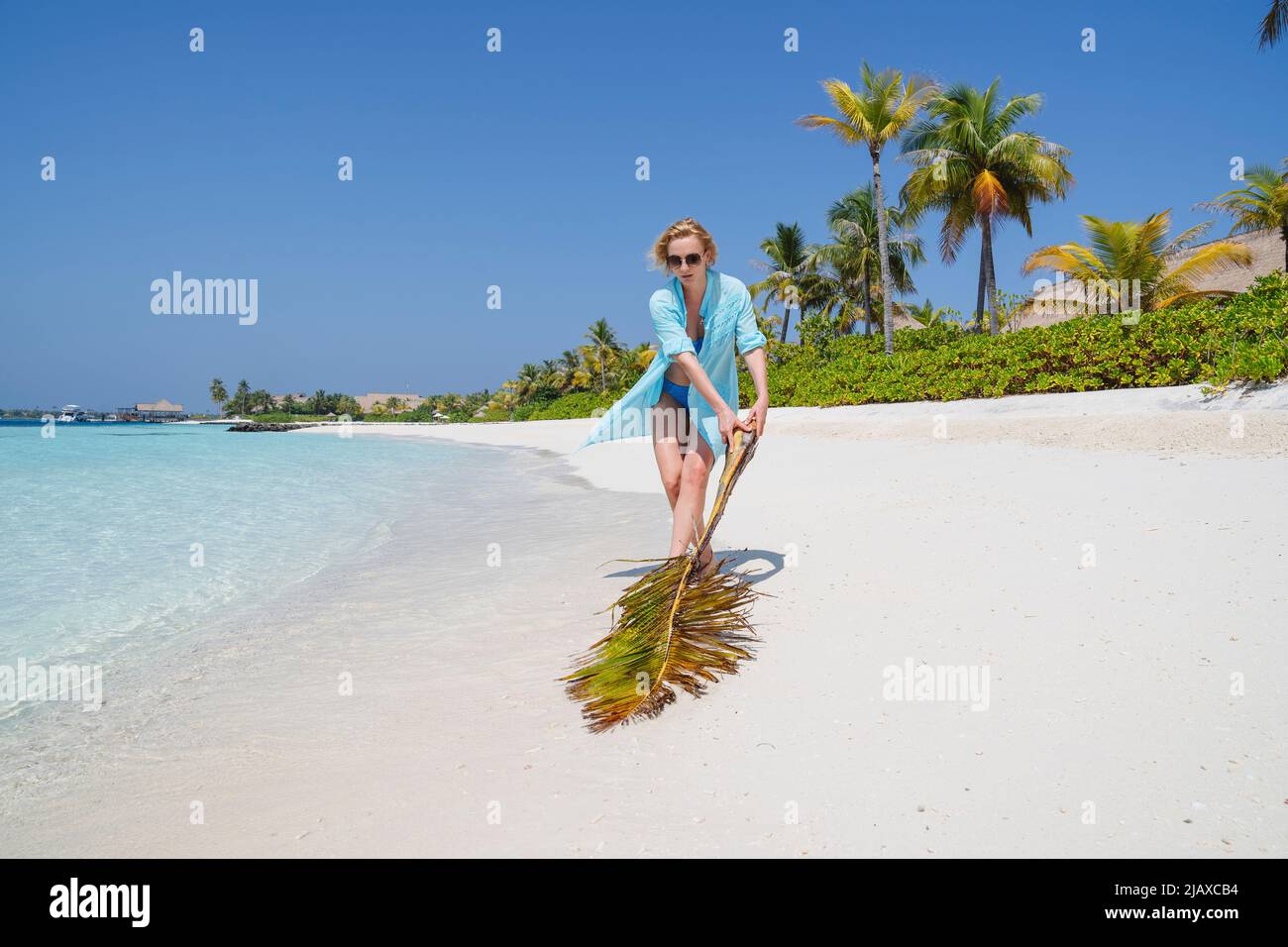 Eine Frau am Strand mit einem großen Zweig einer Palme. Stockfoto