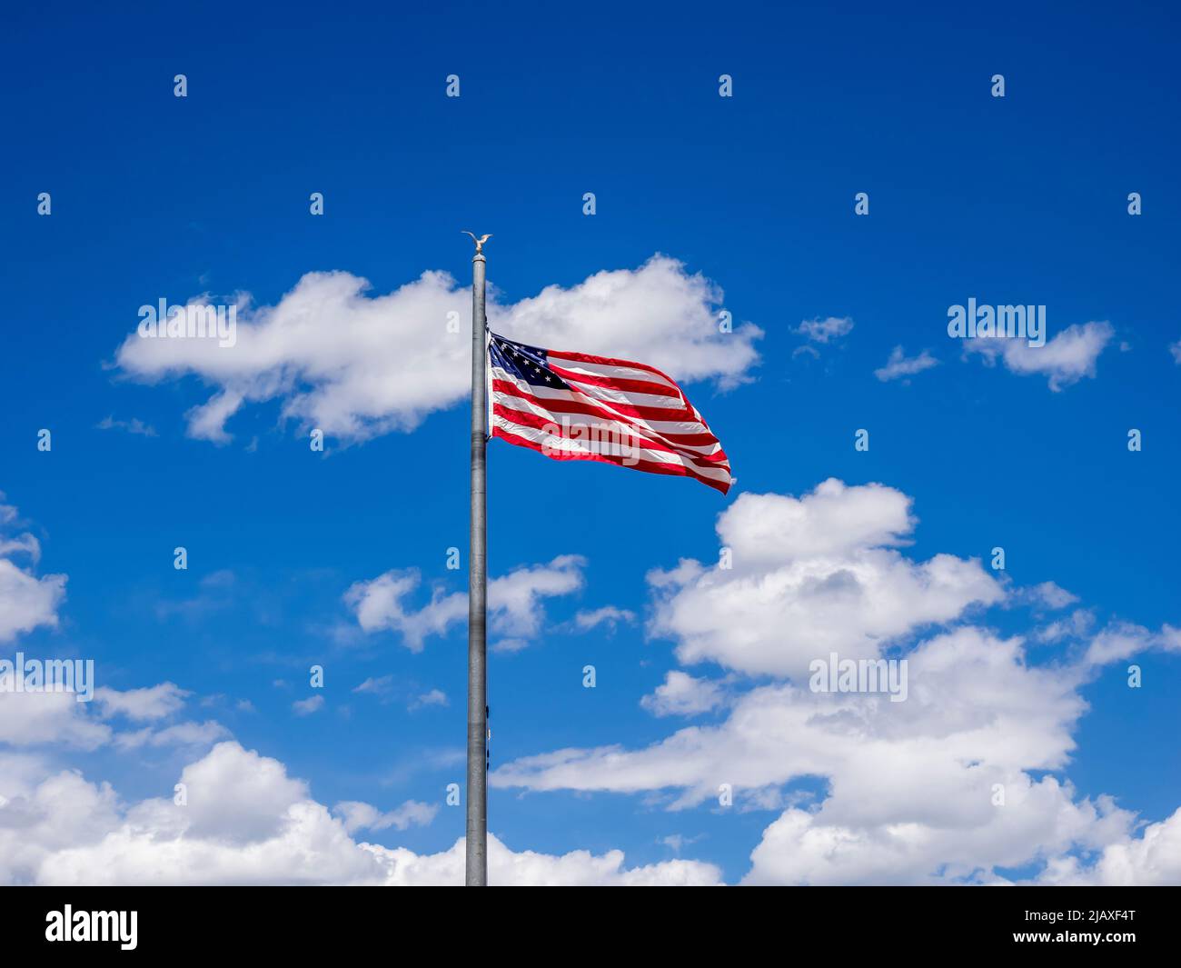 Die amerikanische Flagge, die auf einem Fahnenmast fliegt, hat einen blauen Himmel mit weißen geschwollenen Wolken Stockfoto