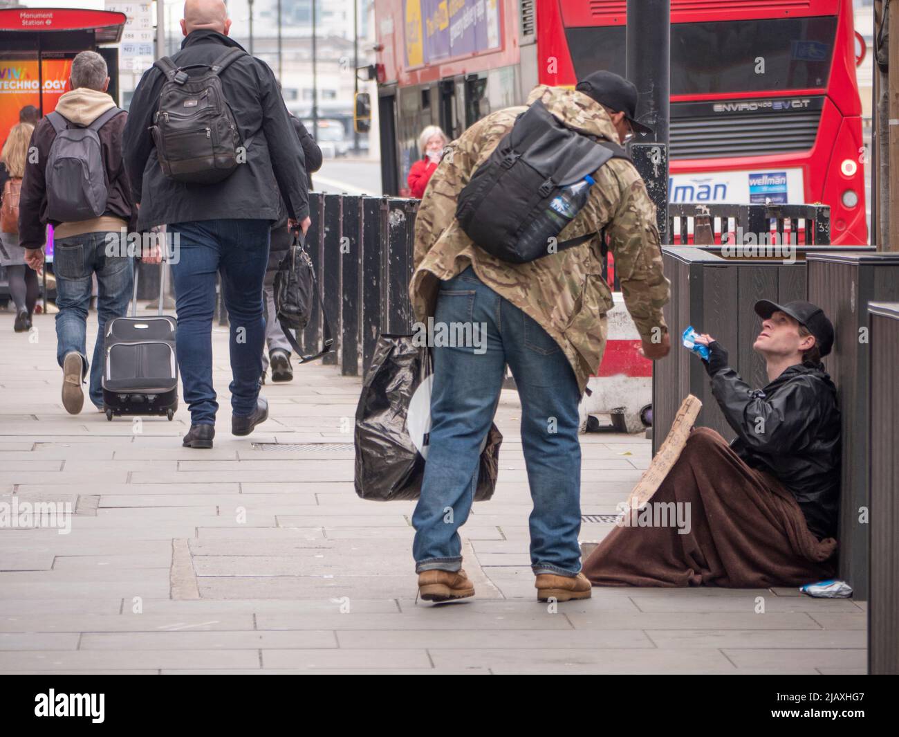 Armut in London, Mitglied der Öffentlichkeit, die sich beugte, um einem Bettler auf der London Bridge mit Decke und Schild Nahrung zu geben Stockfoto
