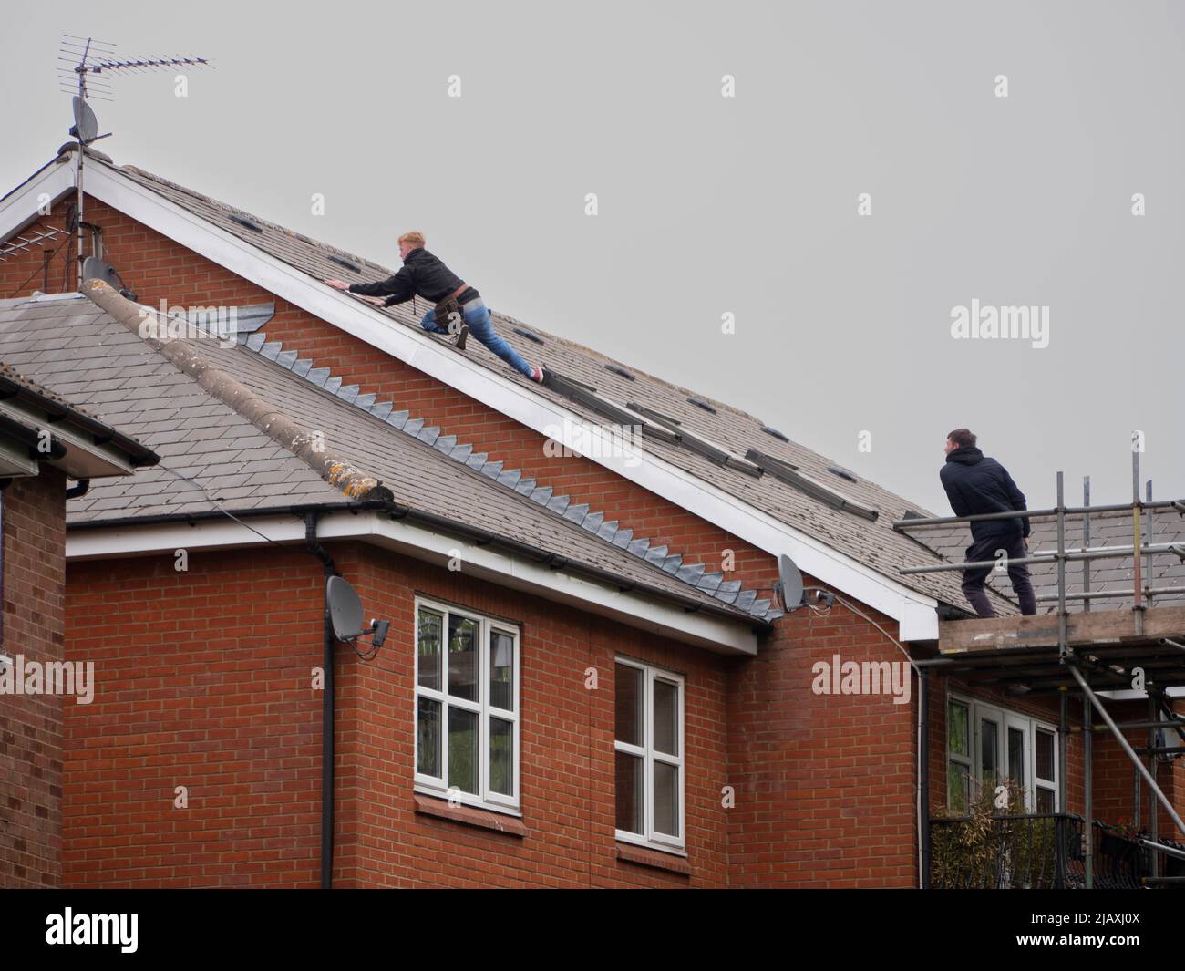 Dachdecker, die in der Höhe arbeiten und Fliesen auf dem Dach im Nordosten Londons befestigen Stockfoto