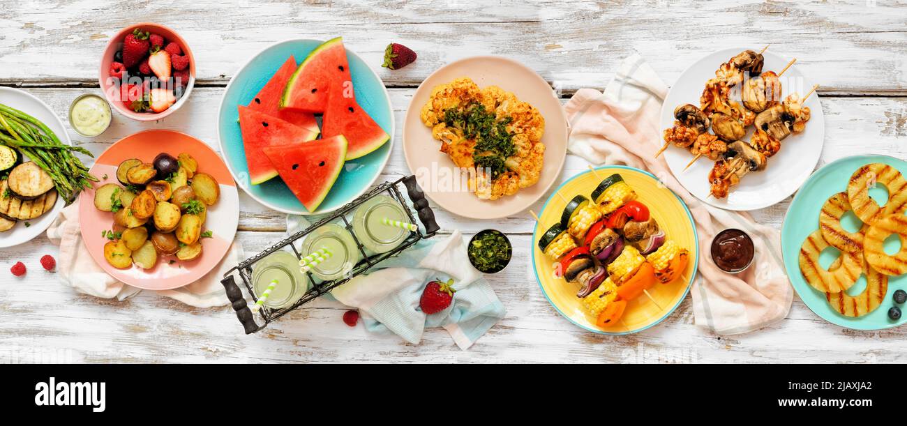 Vegane Sommer bbq oder Picknick-Tischszene.Oben Blick auf einem weißen Holz Banner Hintergrund. Obst, gegrilltes Gemüse, Spieße, Blumenkohlsteak und Limonade Stockfoto