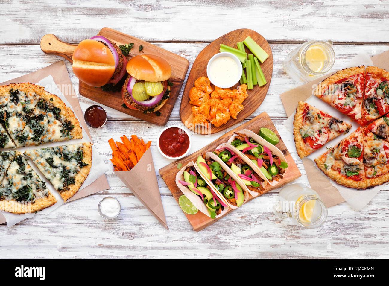 Gesunde Pflanze basiert Fast-Food-Tabelle Szene. Draufsicht auf weißem Holzhintergrund. Pizzas aus Blumenkohlkruste, Bohnenburger, Pilztacos, Paprika na Stockfoto
