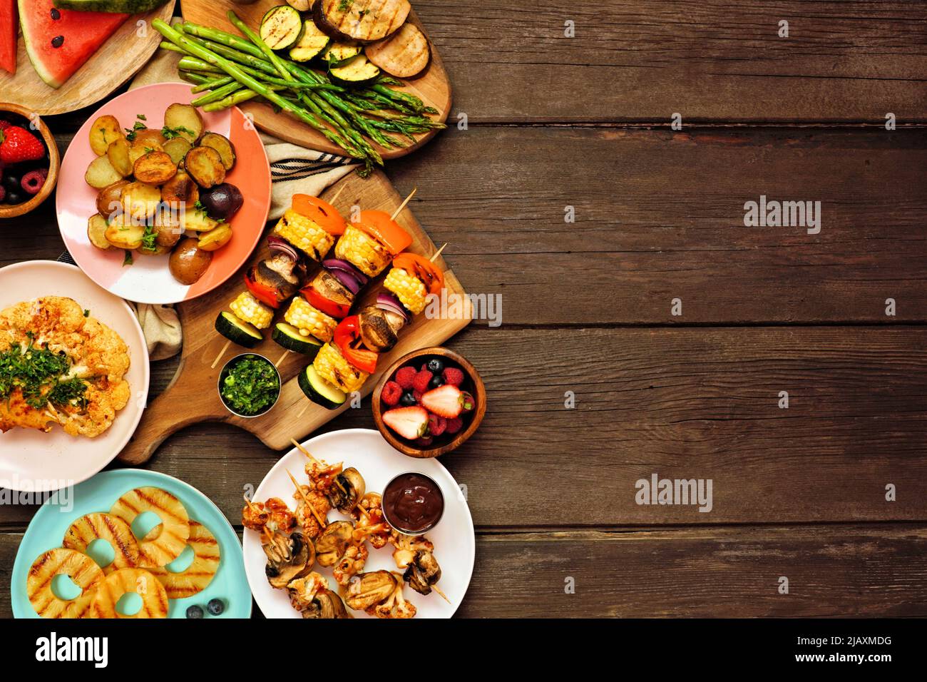 Veganes Sommer-bbq oder Picknick am Rand. Blick über einen dunklen Holzhintergrund. Gegrilltes Obst und Gemüse, Spieße, Blumenkohlsteak und Vegetaria Stockfoto