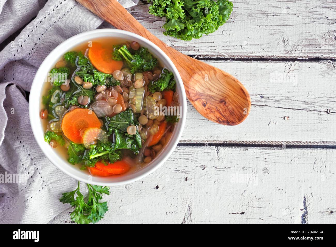 Gesunde Gemüsesuppe mit Grünkohl und Linsen. Deckenansicht Tischszene auf einem rustikalen weißen Holzhintergrund. Stockfoto