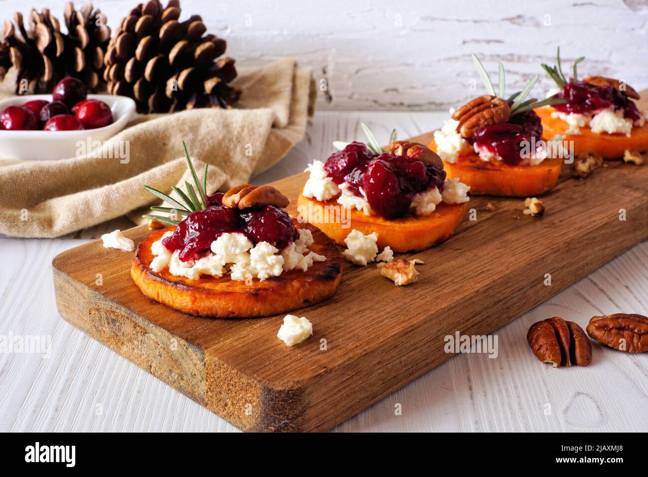 Geröstete Herbst-Süßkartoffel-Crostini-Vorspeisen mit Käse, Preiselbeeren und Pekannüssen auf einer Holzplatte. Tischszene mit weißem Holzhintergrund. Stockfoto