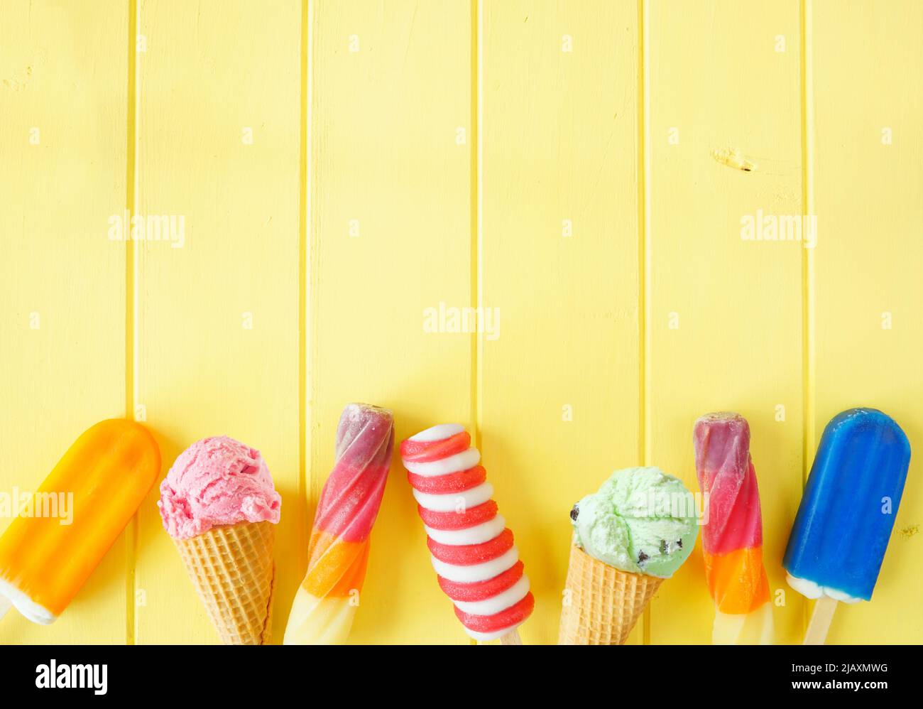 Auswahl an farbenfrohen, gefrorenen Desserts im Sommer. Draufsicht unterer Rand auf einem hellgelben Holzhintergrund. Speicherplatz kopieren. Stockfoto