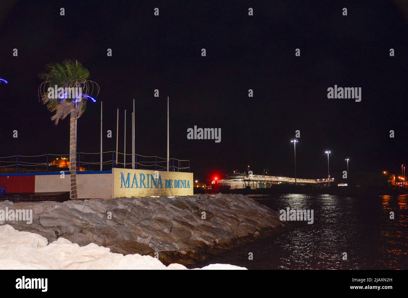 Denia, Alicante, Spanien - 26 2021. Juli: Hafeneingang mit beleuchtetem 'Marina de Denia' Schriftzug auf einer weißen Wand in der Nacht mit einem blau beleuchteten pal Stockfoto