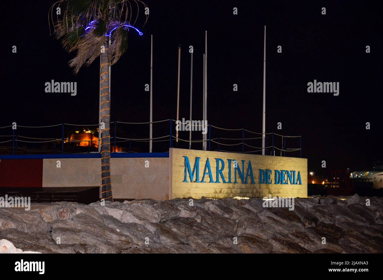 Denia, Alicante, Spanien - 26 2021. Juli: Hafeneingang mit beleuchtetem 'Marina de Denia' Schriftzug auf einer weißen Wand in der Nacht mit einem blau beleuchteten pal Stockfoto
