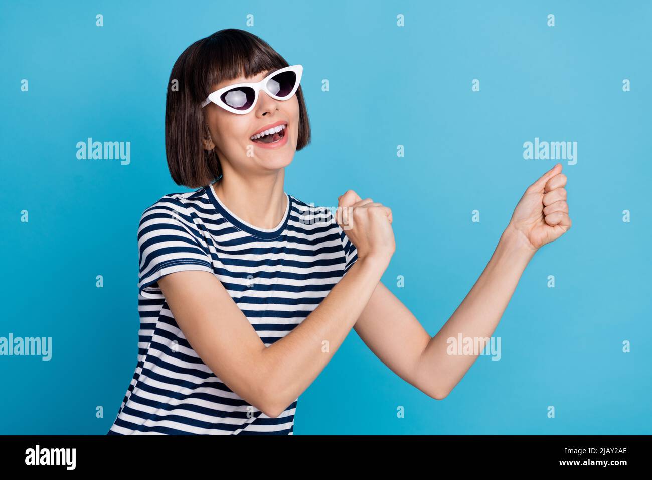 Foto von funky Brünette junge Dame Tanz tragen Brille gestreiftes T-Shirt auf blauem Hintergrund isoliert Stockfoto