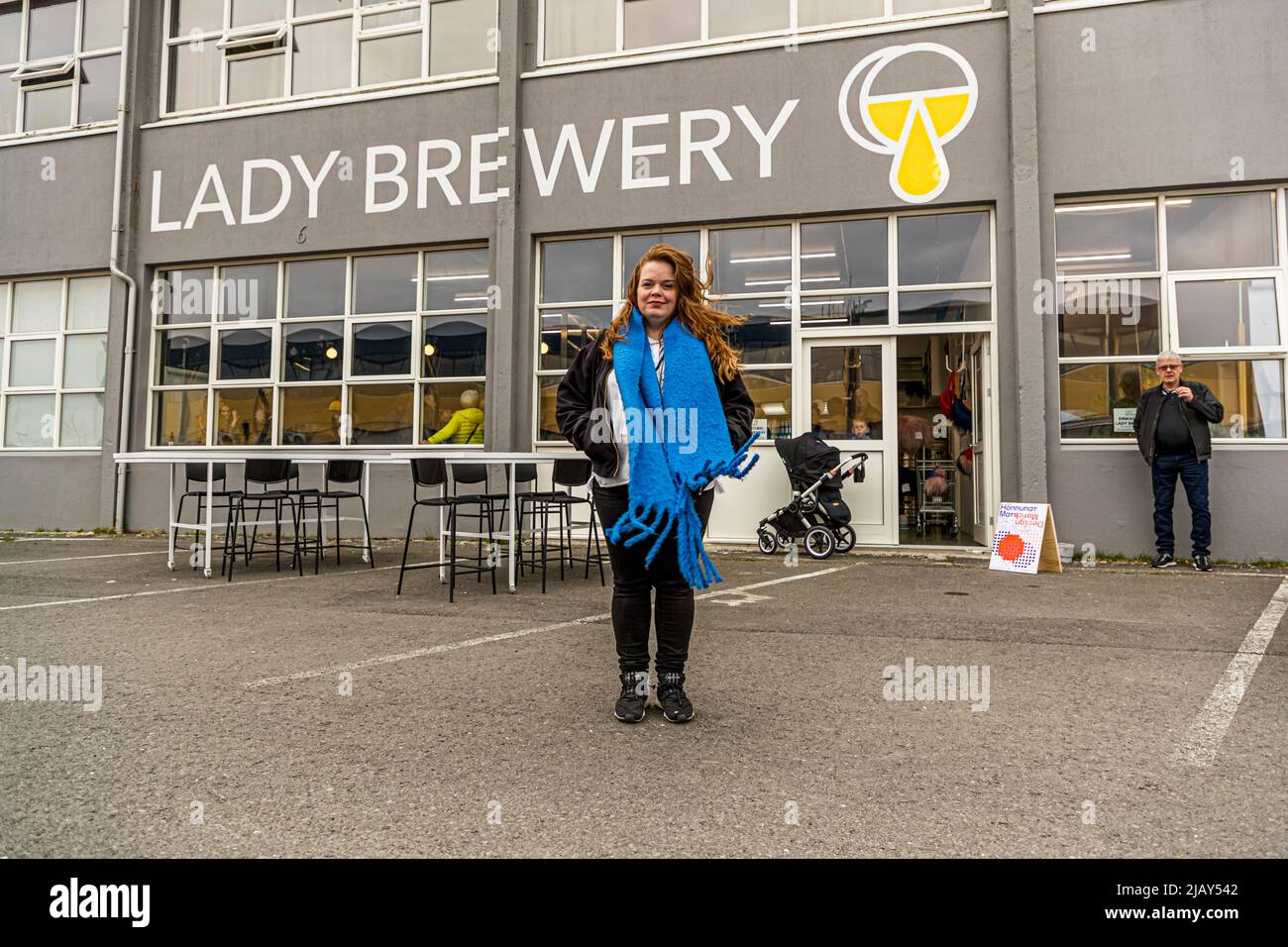 Meisterbrauerin Þórey Björk Halldórsdóttir posiert mit einem hellblauen, flauschigen Schal vor dem Schild ‚Lady Brewery‘ im Hauptsitz der gleichnamigen Brauerei im Hafenviertel Grandi von Reykjavík, Island. Der Anlass markiert eine Design-March-Kooperation 2022 zwischen der von Meisterbrauerin Þórey Björk Halldórsdóttir gegründeten Brauerei und Gæla, die zur Biersorte ‚On A Roll‘ mit ihrem gestrickten Flaschenetikett führte. Stockfoto