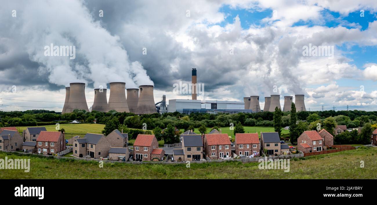 Häuser im Schatten eines großen Industriekraftwerks, die die Atmosphäre und die umliegenden Gebiete mit Kohlendioxid in einer Umgebung und Soci verschmutzen Stockfoto
