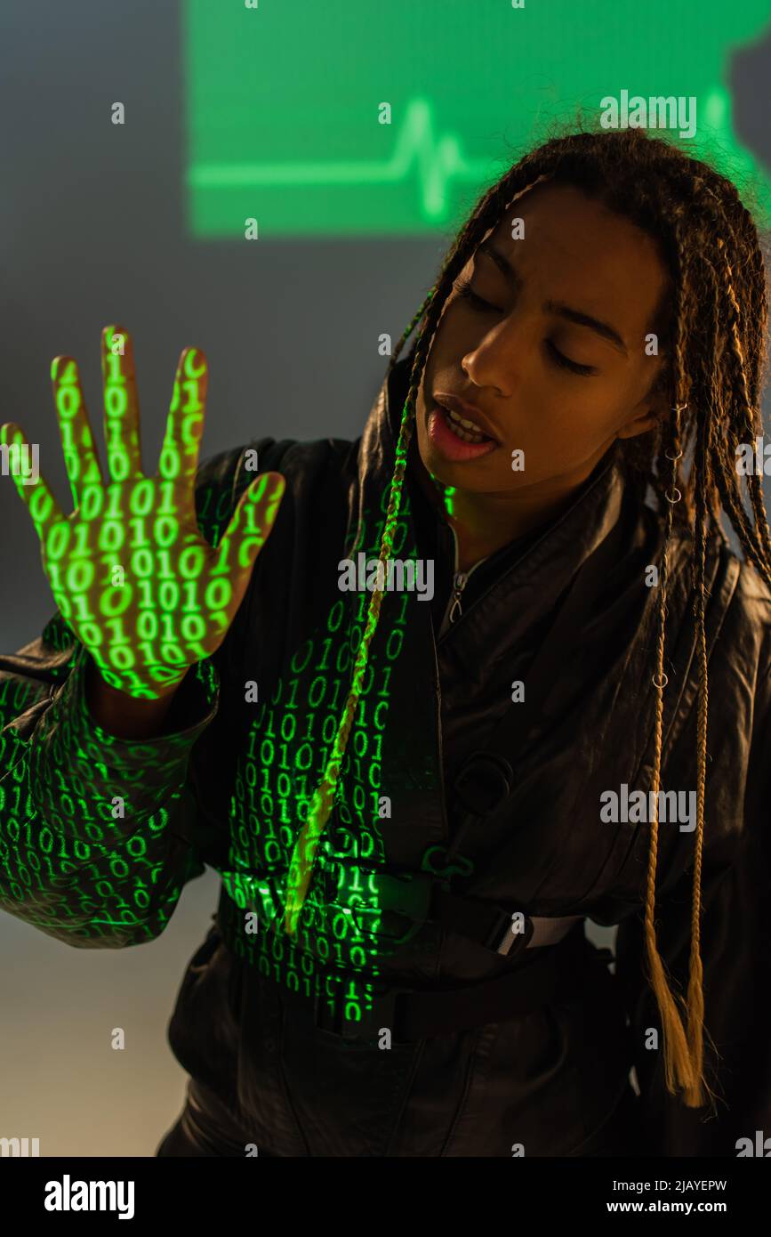 afroamerikanische Frau in Lederjacke mit Projektion von Computercode auf grauem Hintergrund Stockfoto