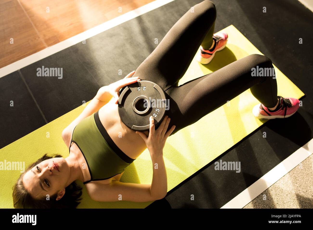 High-View-Bild einer jungen Sportlerin, die ihr Gewicht auf den Bauch legt und die Trainingspresse auf die Trainingsmatte drückt Stockfoto