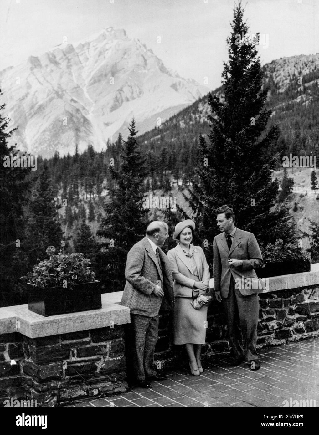 König und Königin in den Rockies -- der König und die Königin mit Mr. Mackenzie King auf der Terrasse des Banff Springs Hotels, zeigt Cascade Mountain im Hintergrund. Dem König und der Königin wurde eine Pause von den ziemlich anspruchsvollen Aufgaben ihrer Tour gewährt, als sie eine kurze Pause im berühmten Banff Springs Hotel in den kanadischen Rockies genossen. 5. Juni 1939. (Foto von Topical Press). Stockfoto