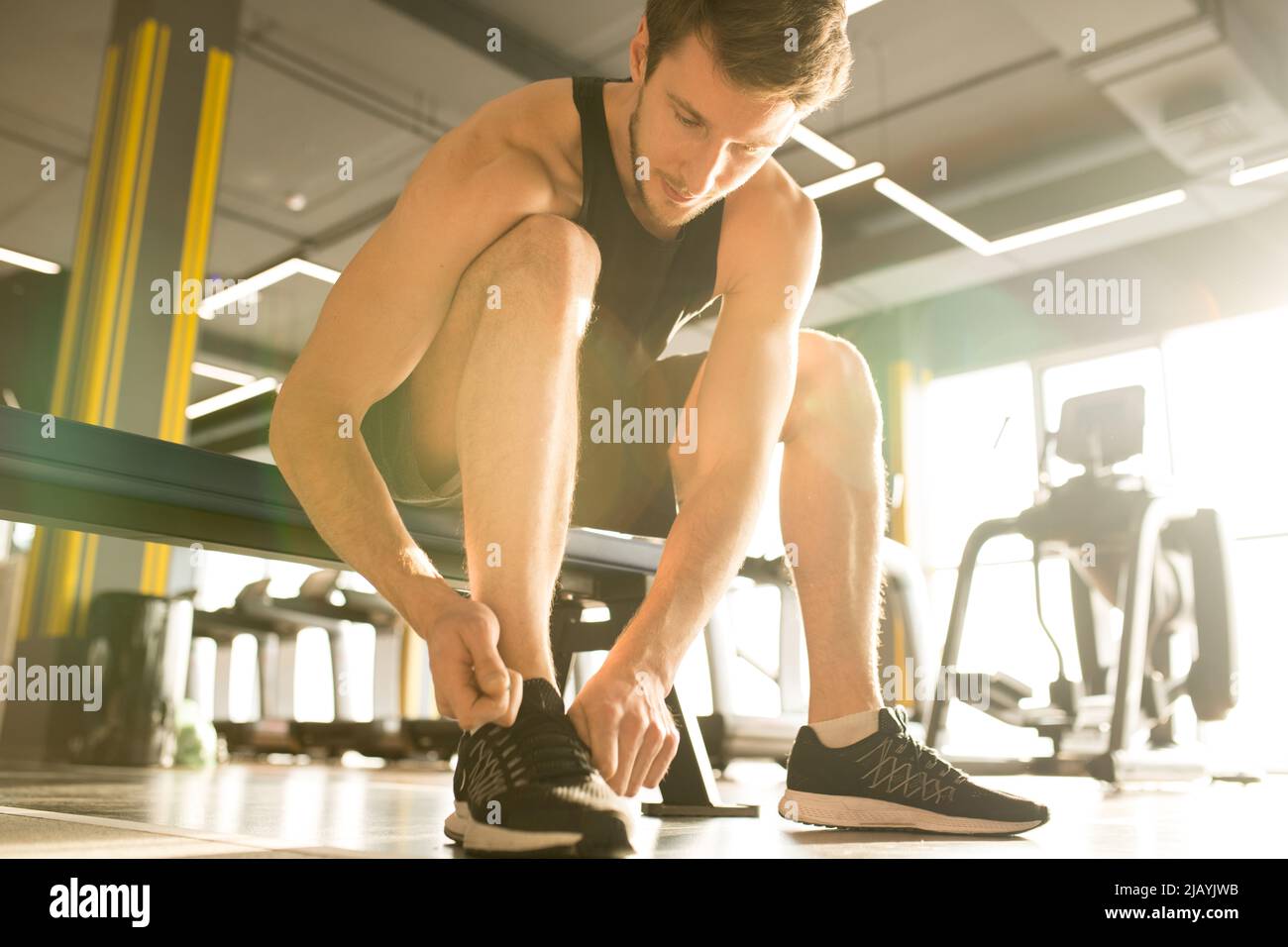 Junger Mann sitzt auf der Bank im Fitnessstudio und tieing die Schnürsenkel auf seine Turnschuhe Stockfoto