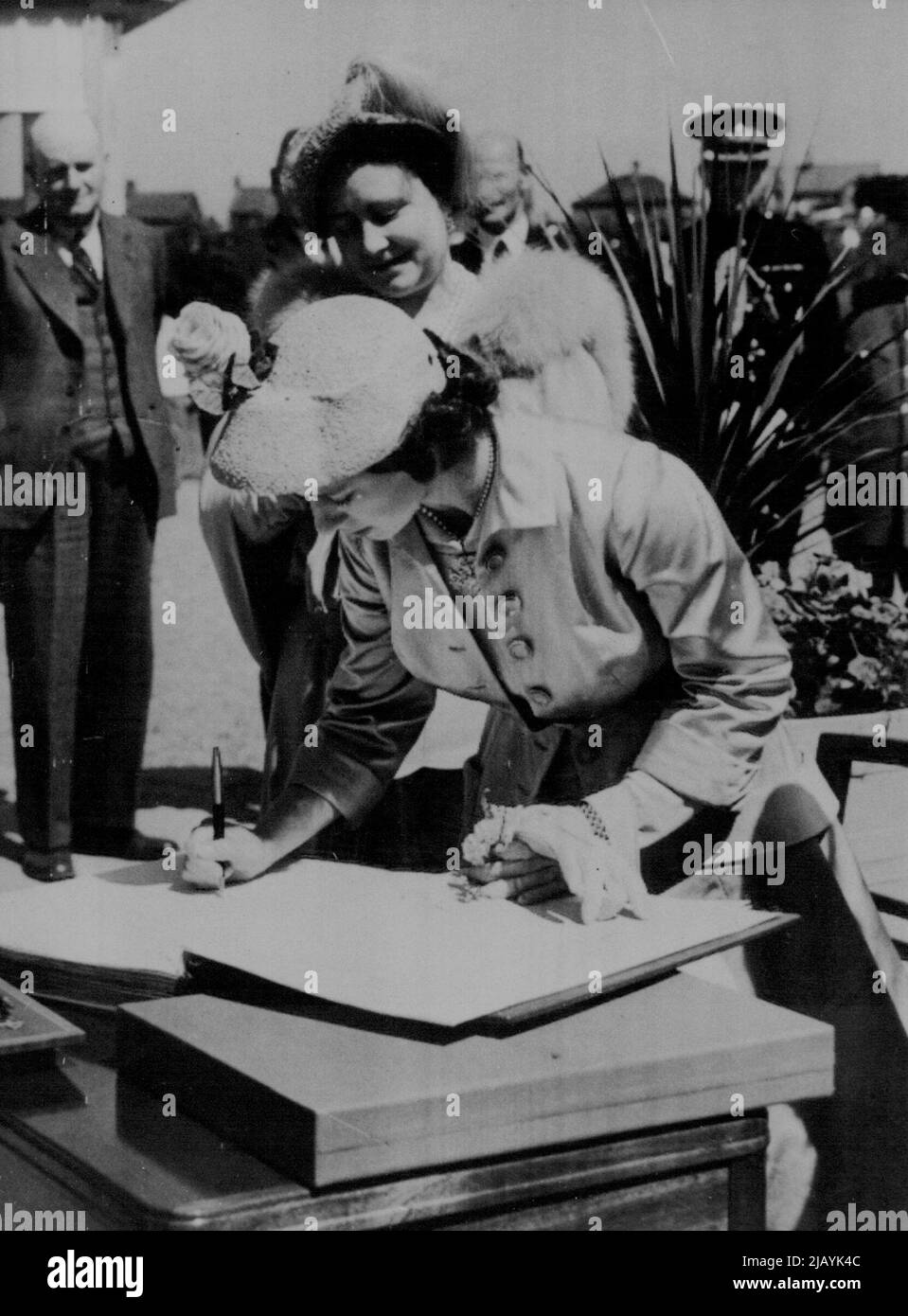 Prinzessin Margaret signiert Festivalbuch - Prinzessin Margaret, in einem sommerlichen Ensemble mit einem Hahnmütze, signiert das Besucherbuch beim Castlereagh (Belfast) Festival of the Britain Exhibition Factory während der Royal Tour durch Nordirland heute (Freitag). Zuschauen ist die Queen, die ein pulverblaues Seidenkleid mit passender Mütze trägt. Der Seidenmantel von Prinzessin Margaret ist in Austerngrau gehalten und wird über einem rosa Seidenkleid getragen. Ihr passender Hut ist aus rosafarbenem Stroh, der mit einer Neigung nach vorne getragen wird. 01. Juni 1951. Stockfoto