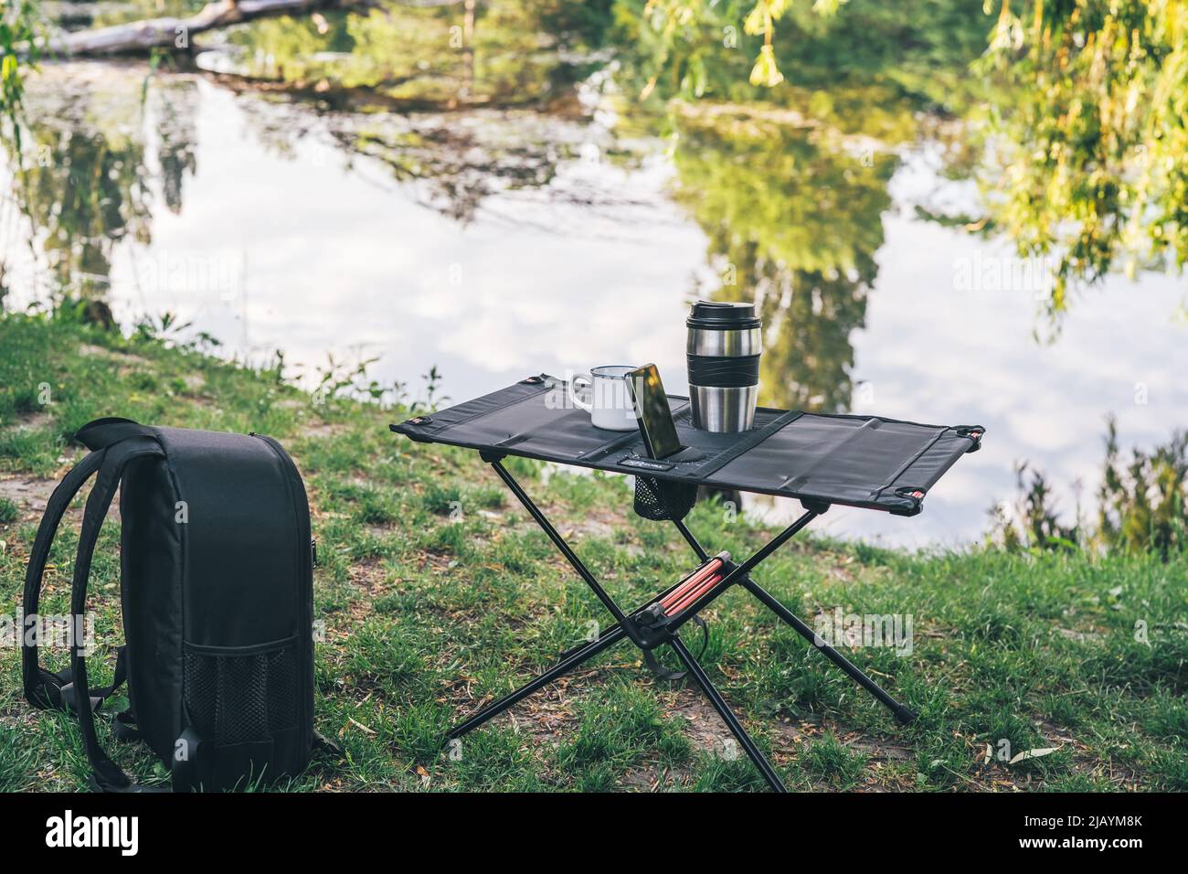 Campingtisch mit Tasse Kaffee und Smartphone im Freien. Technologie für den täglichen Gebrauch. Malerische Landschaft. Freizeit- und Reisekonzept Stockfoto