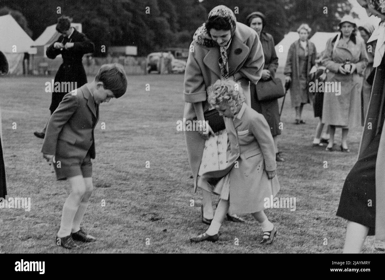 The Royal Family at Polo Tournament -- nach dem Vorbild von Königin Elizabeth am Vortag helfen Prinz Charles und Prinzessin Anne, den von den Poloponies in der Pause angepfropften unplatzierten Rasen zu beschreiten. H.M. die Königin mit ihren beiden Kindern Preise Charles und Prinzessin Anne nahmen an dem Polo-Turnier Teil, das jetzt auf Smith's Lawn im Windsor Great Park stattfindet, wo sie den Herzog von Edinburgh für eines der konkurrierenden Teams spielen sahen. 15. Juni 1955. (Foto: Sport & General Press Agency, Limited). Stockfoto