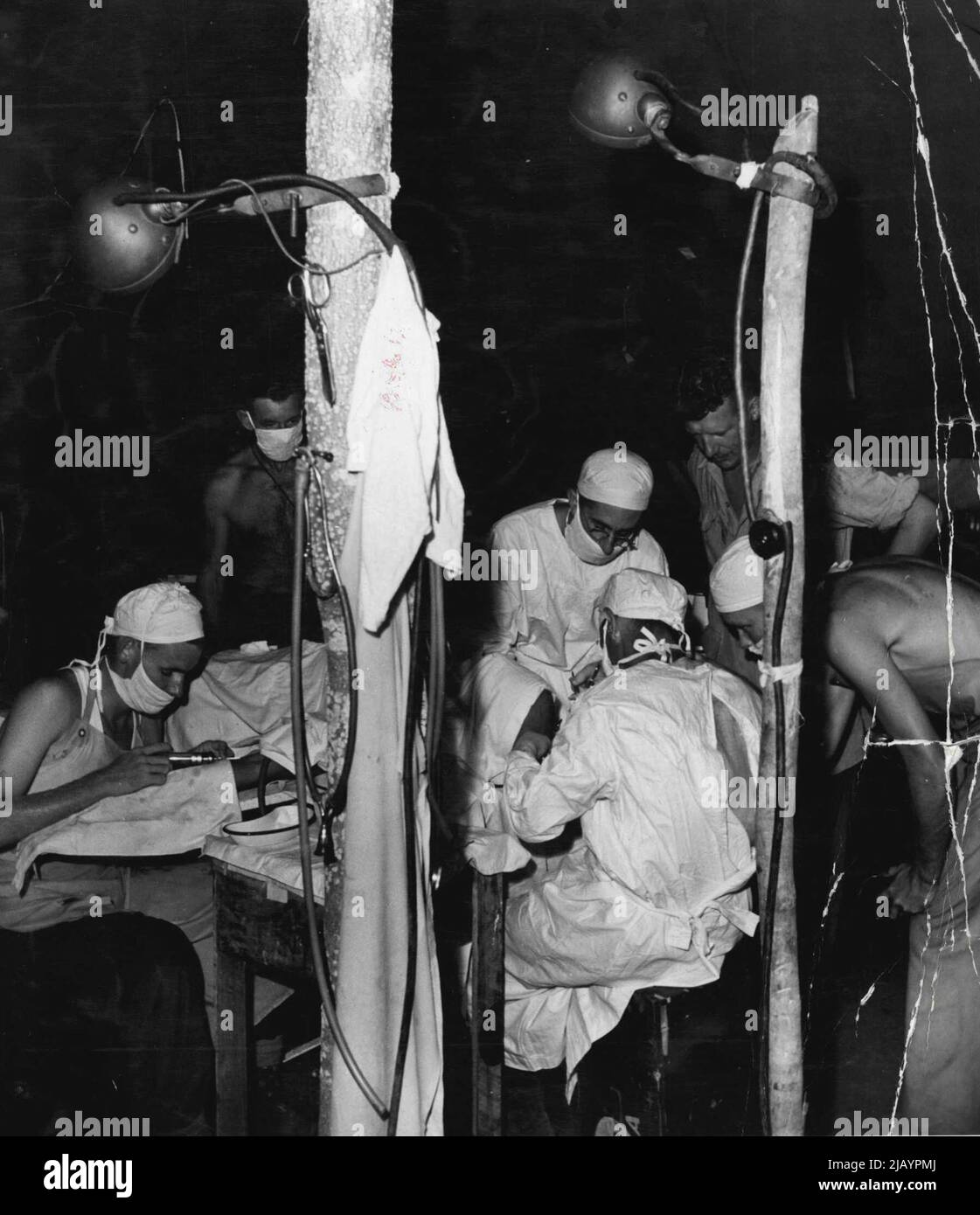 Dies ist am Hauptsitz eines mobilen OP-Teams, der vorwärtssten medizinischen Stelle im Kampfgebiet. Ein Australier, der am Kopf verletzt wurde, wird einer Operation unterzieht. Unterstützung des medizinischen Offiziers sind links nach rechts Pte. C. Bingham aus Townsville, Qld, Sgt. G. Smith von Edgecliff, N.S.W. und Pte. S. Dow von Mackay Qld. 1. November 1943. Stockfoto