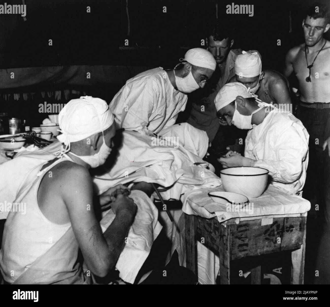 Dies ist am Hauptsitz eines mobilen OP-Teams, der vorwärtssten medizinischen Stelle im Kampfgebiet. Ein Australier, der am Kopf verletzt wurde, wird einer Operation unterzieht. Unterstützung des medizinischen Offiziers sind links nach rechts Pte. C. Bingham aus Townsville, Qld, Sgt. G. Smith von Edgecliff, N.S.W. und Pte. S. Dow von Mackay Qld. 13. Januar 1944. Stockfoto