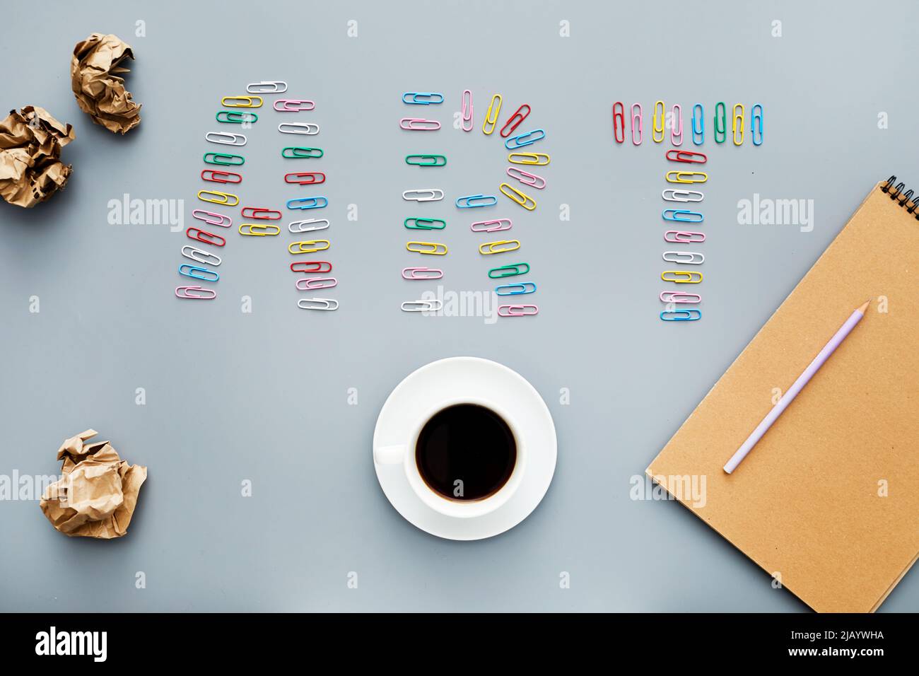 High-Angle-Ansicht des kreativen Arbeitsplatzes mit knirschtem Papier, Tasse schwarzem Kaffee, Notizblock und Bleistift, Kunstbeschriftung aus bunten Büroklammern Stockfoto