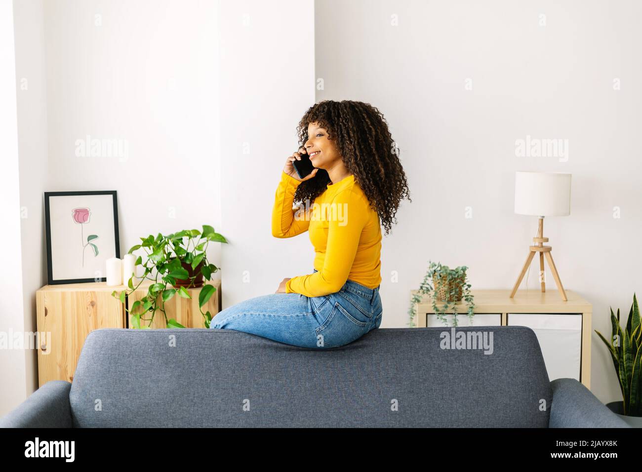Glückliche junge Frau, die ein Mobiltelefon benutzt, während sie sich zu Hause ausruhte Stockfoto